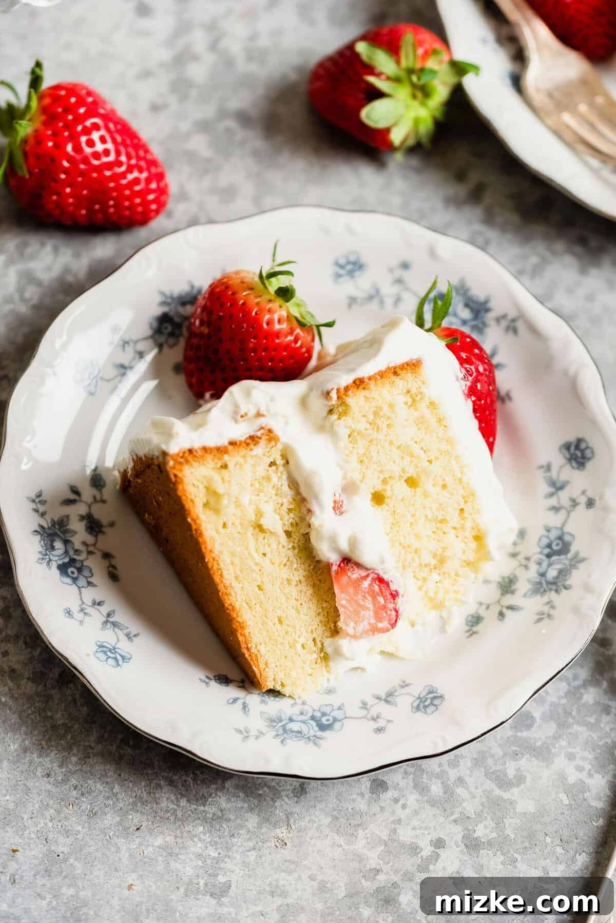 Luscious Strawberry Sponge 3 A single slice of strawberry sponge cake expertly plated, garnished with additional fresh strawberry halves and a dollop of whipped cream, showcasing its delicate layers.