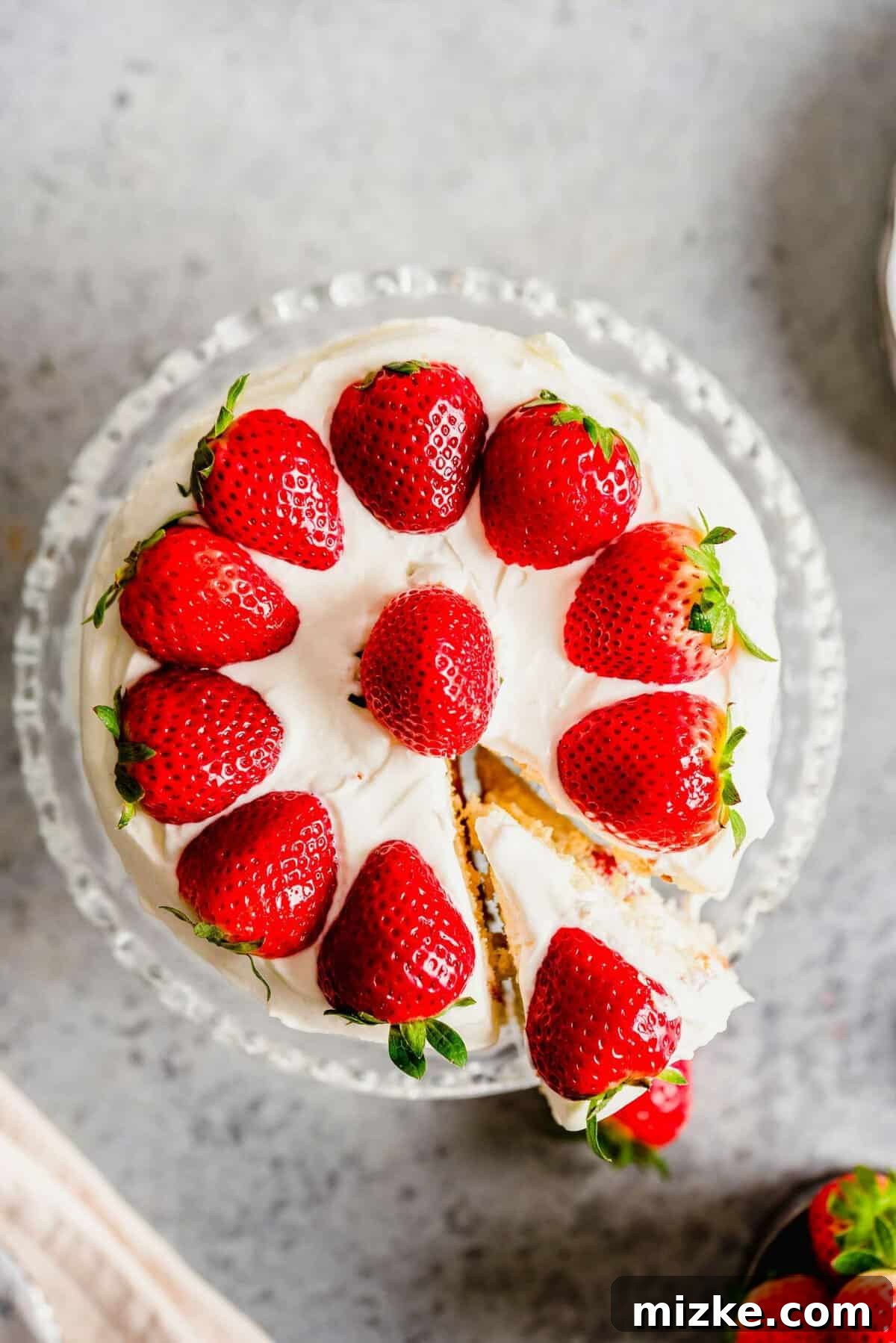 Luscious Strawberry Sponge 4 An overhead shot of the strawberry sponge cake, artfully decorated with whole and sliced strawberries. One slice is being carefully removed, highlighting the layers.