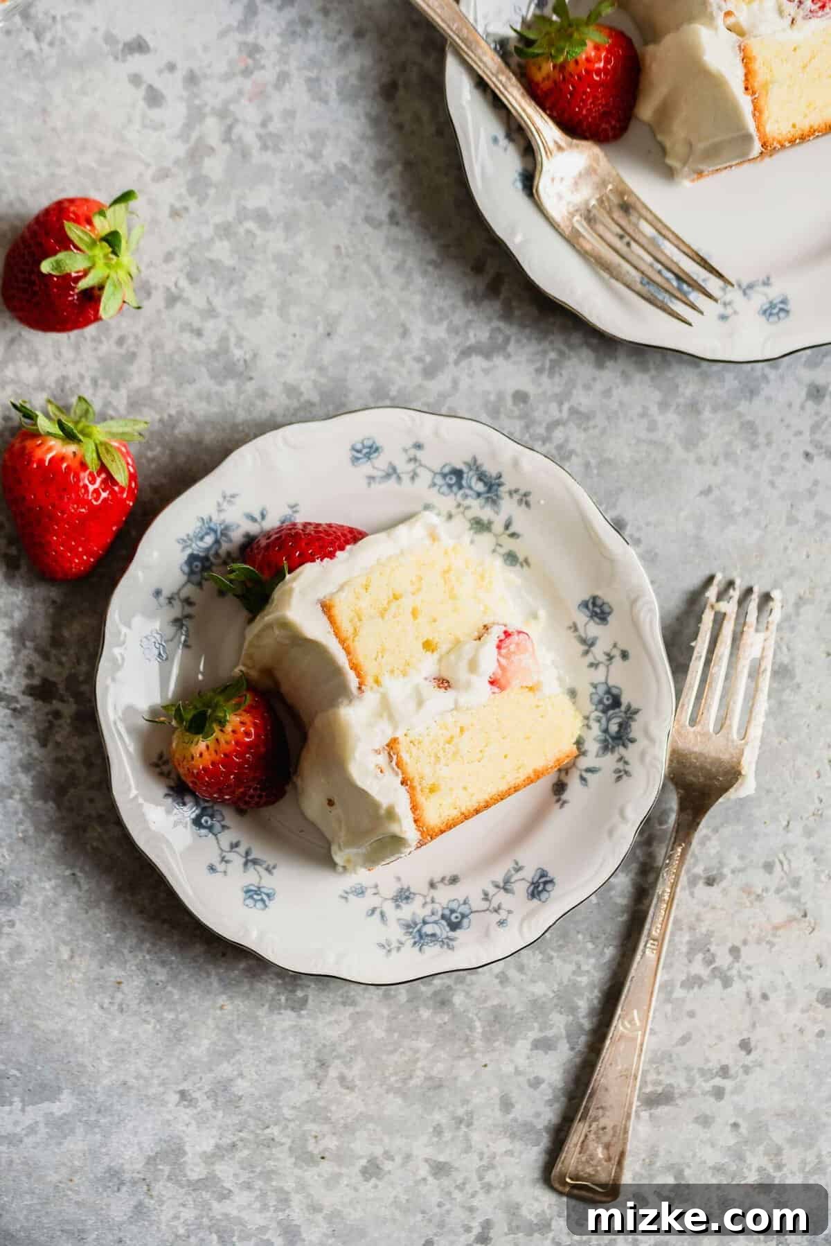 Luscious Strawberry Sponge 5 Two plates, each holding a slice of strawberry sponge cake, elegantly garnished with fresh strawberries, presented from an overhead perspective.