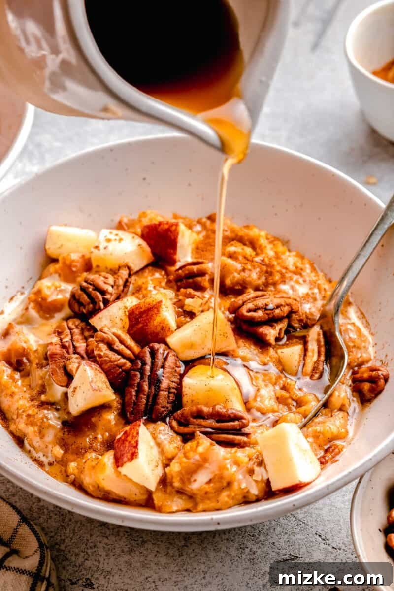 Overnight Apple Cinnamon Slow Cooker Oats 3 maple syrup being poured on apple cinnamon oats in a white bowl, enhancing the presentation