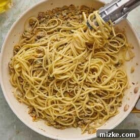 White Wine Clam Linguine 9 A pan of spaghetti with clams being served with tongs. Grated cheese sits in a bowl nearby.