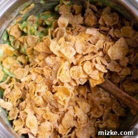Crunchy Wreath Delights 12 Cornflake cereal being folded into the green marshmallow mixture.
