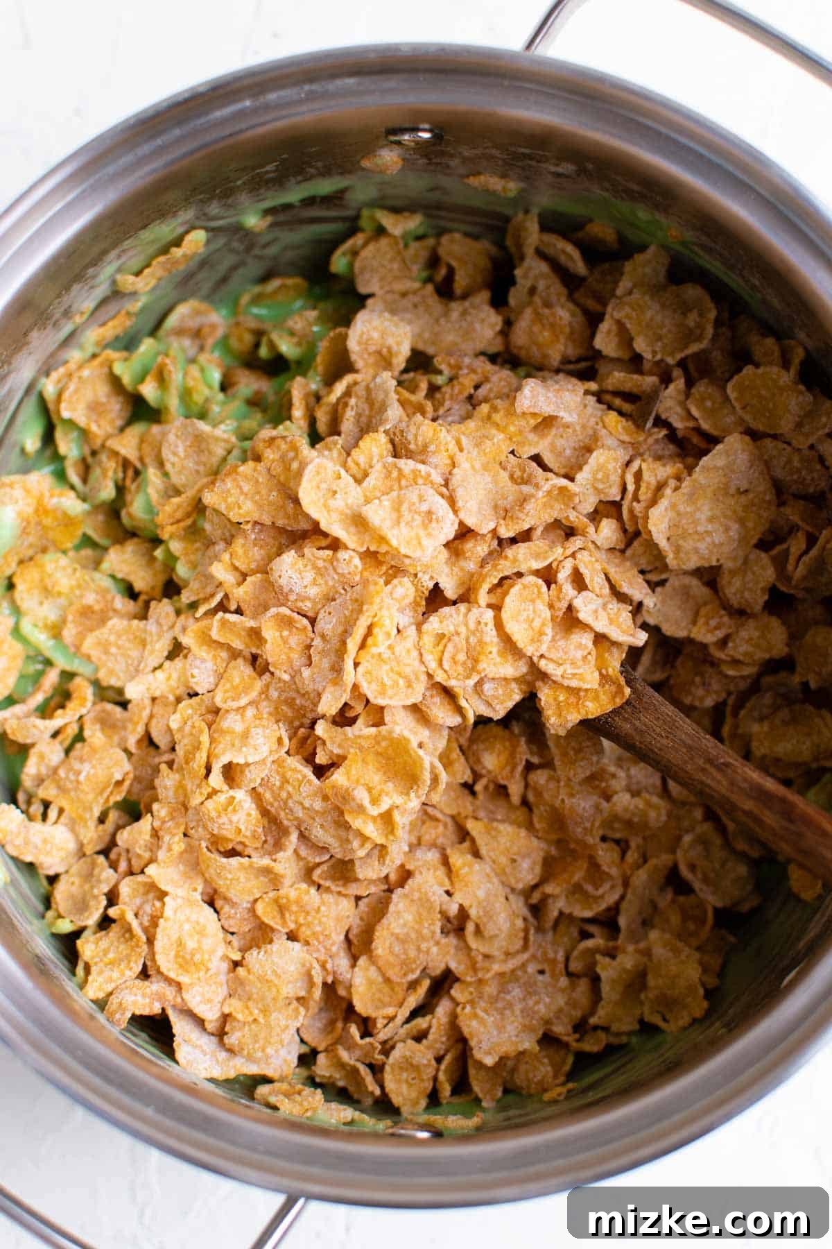 Crunchy Wreath Delights 6 Crunchy cornflake cereal being gently mixed into the vibrant green marshmallow mixture, ensuring even coating.