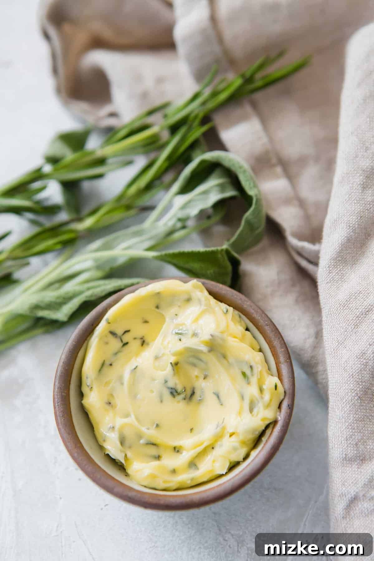 Gourmet Herb Butter 3 Closeup of small bowl filled with compound butter with sprigs of herbs in background