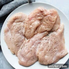 French Onion Smothered Chicken 4 raw thin cut chicken breasts seasoned with salt and pepper on a white plate