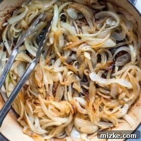 French Onion Smothered Chicken 6 onions being caramelized in a dutch oven with metal tongs in the pot