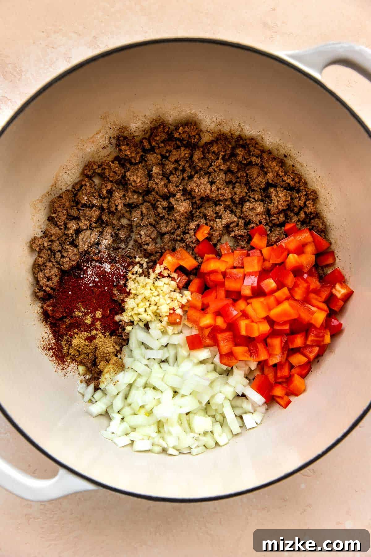 Crumbled ground beef with seasonings and vegetables in a cast iron skillet, mid-cooking process.