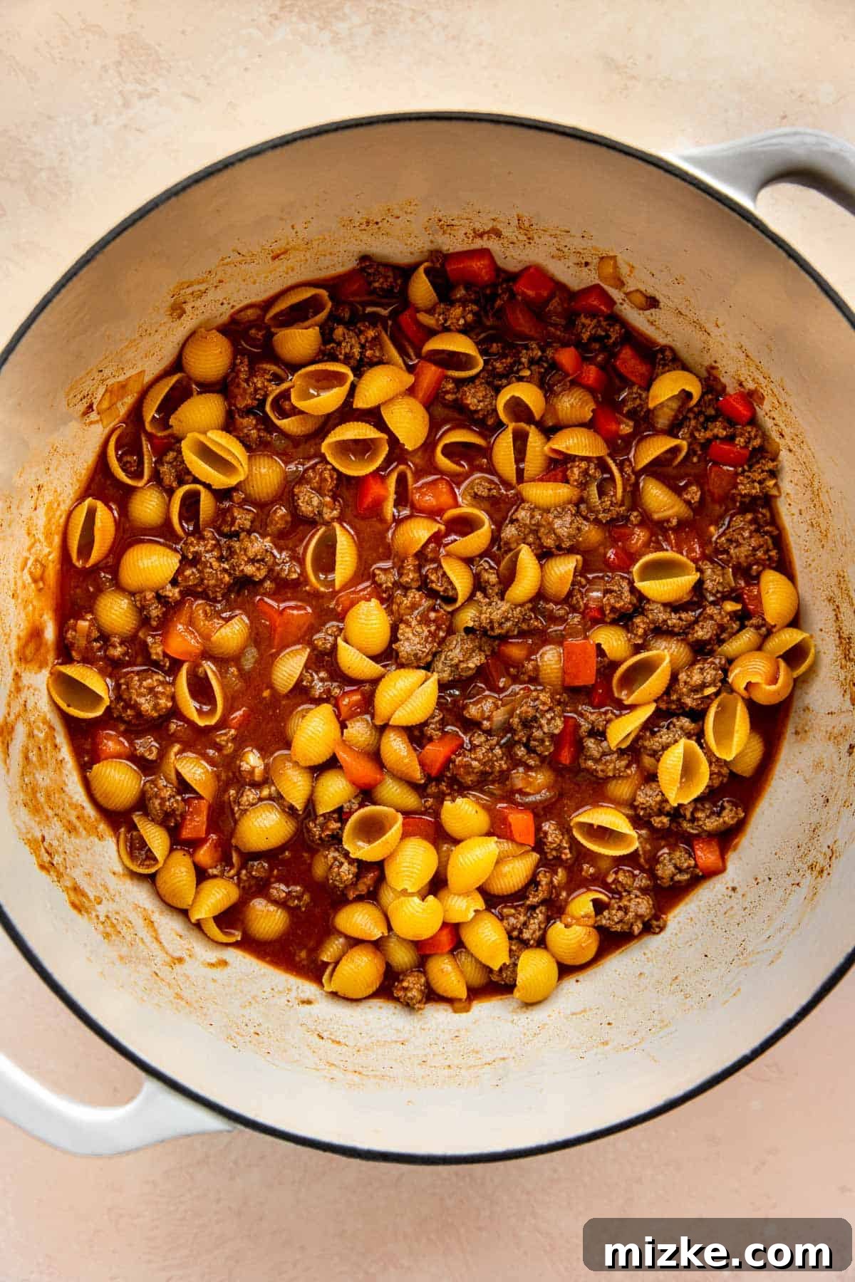 Beef broth and dried pasta shells added to the ground beef mixture in the cast iron skillet, before simmering.