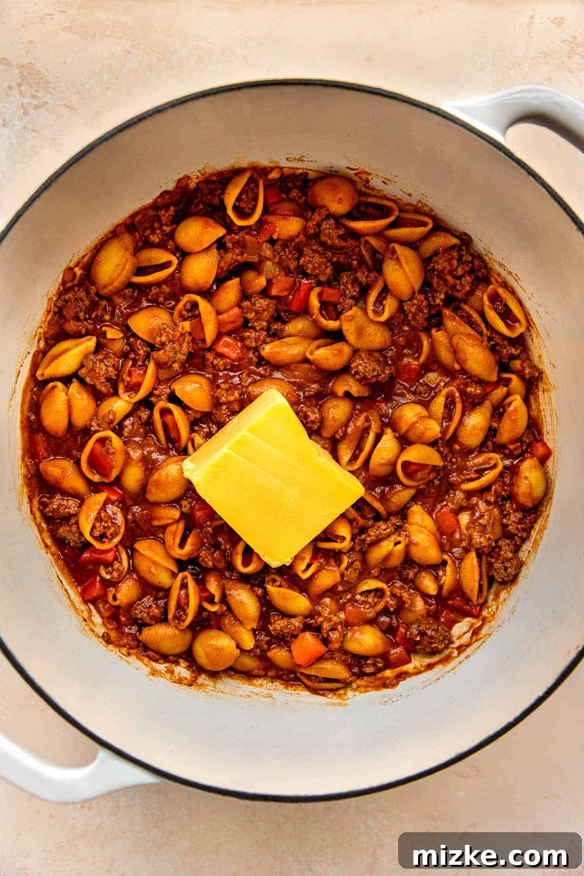 A block of Velveeta cheese being added to the finished pasta dish for ultimate creaminess.