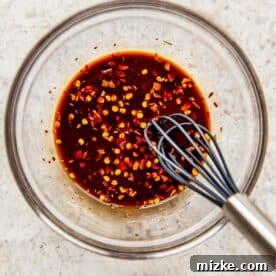 kung pao chicken sauce in a clear bowl with a metal whisk
