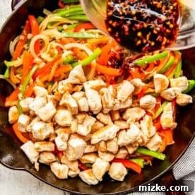 chicken and vegetables in a cast iron skillet with sauce being drizzled on top