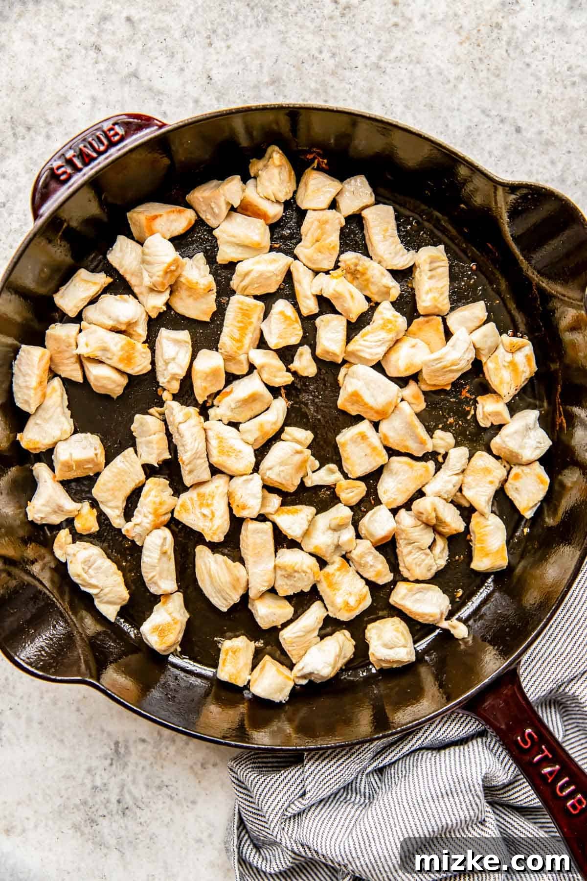 Spicy Szechuan Peanut Chicken 5 Browned chicken pieces sizzling in a cast iron skillet during the cooking process.