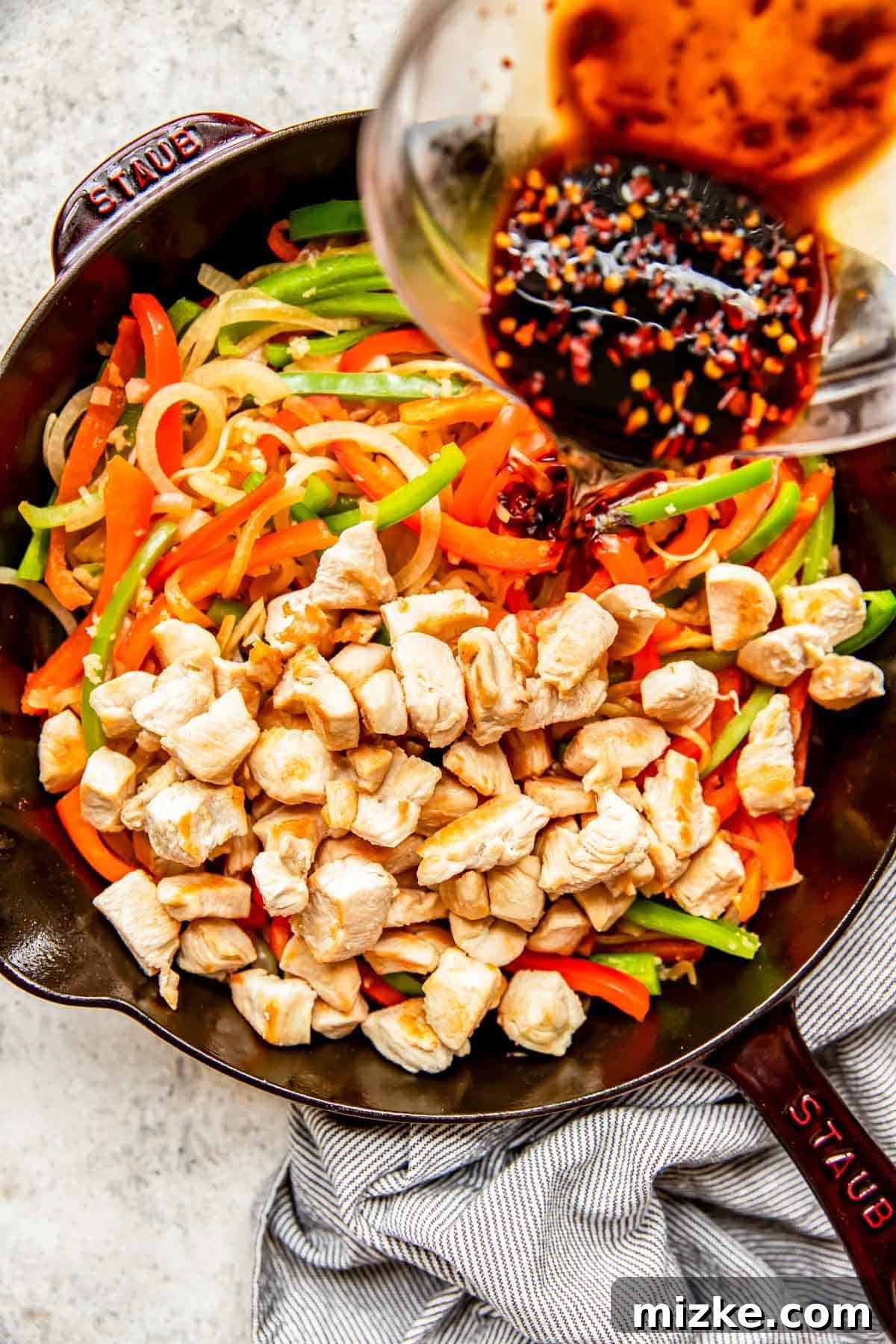 Spicy Szechuan Peanut Chicken 7 Chicken and vegetables being tossed in a cast iron skillet as the thickened Kung Pao sauce is drizzled over them.