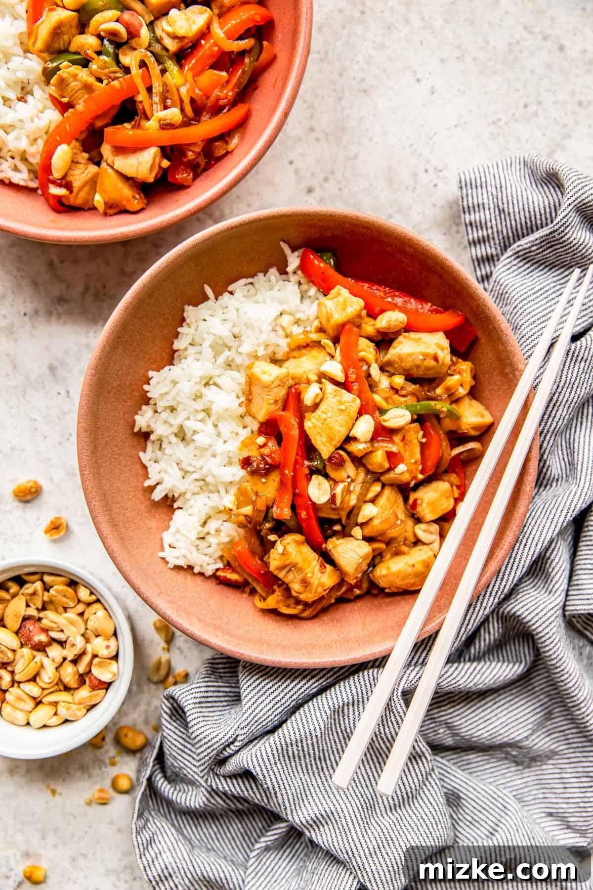 Spicy Szechuan Peanut Chicken 8 A bowl of Kung Pao Chicken and white rice, accompanied by plastic chopsticks, ready for a delicious meal.