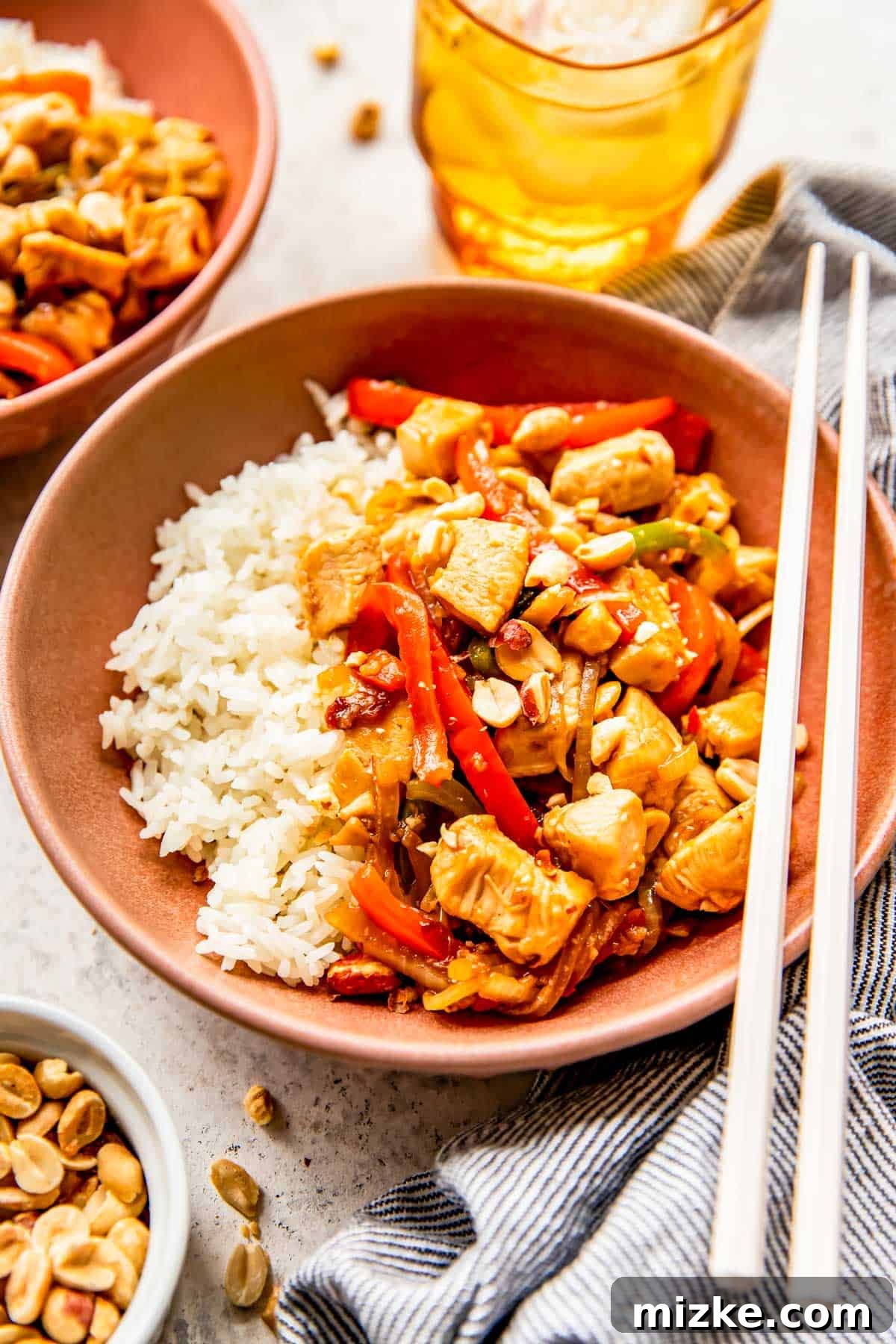 Spicy Szechuan Peanut Chicken 9 A vibrant bowl of Kung Pao Chicken served with fluffy white rice and plastic chopsticks.