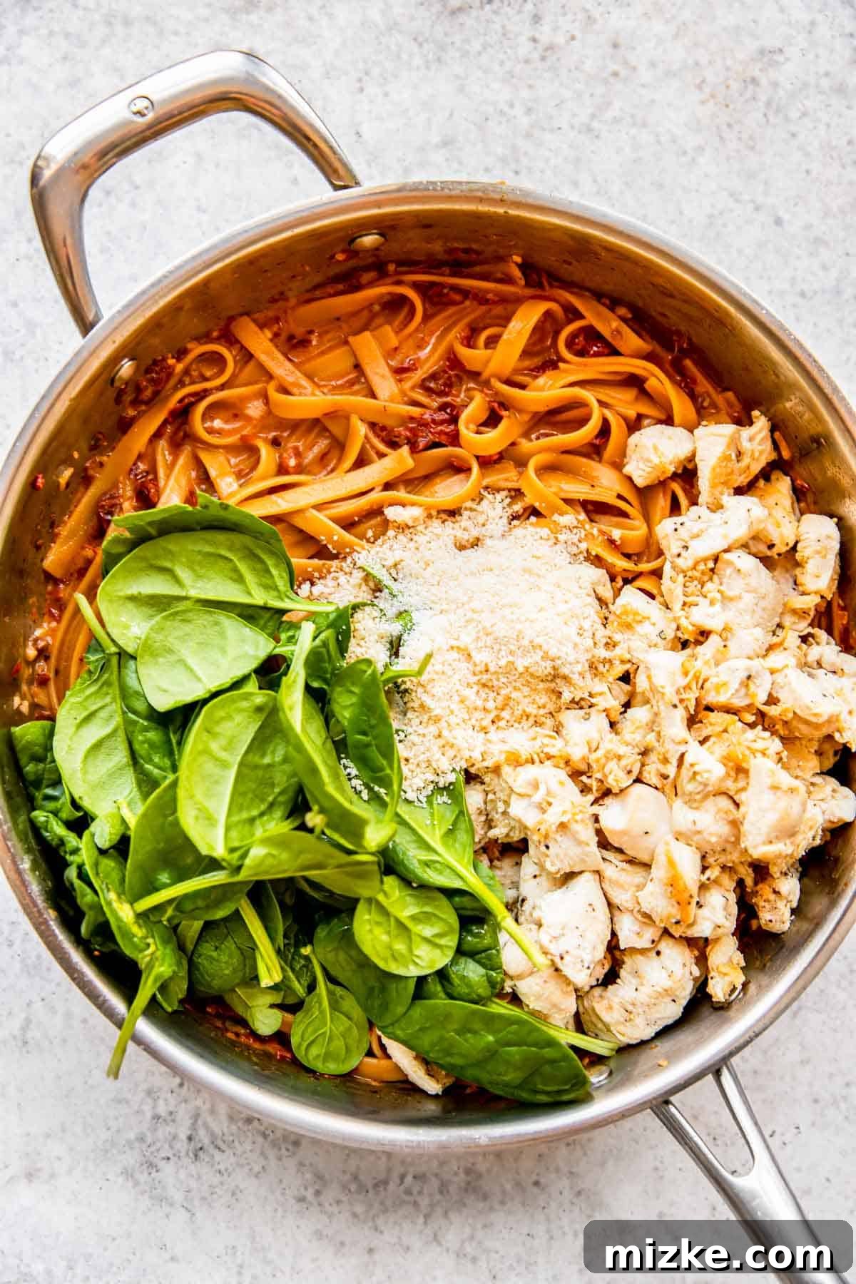 Sun-Kissed Skillet Chicken Pasta 11 Fresh spinach, grated Parmesan cheese, and the previously cooked chicken being added to the finished pasta in the stainless steel skillet