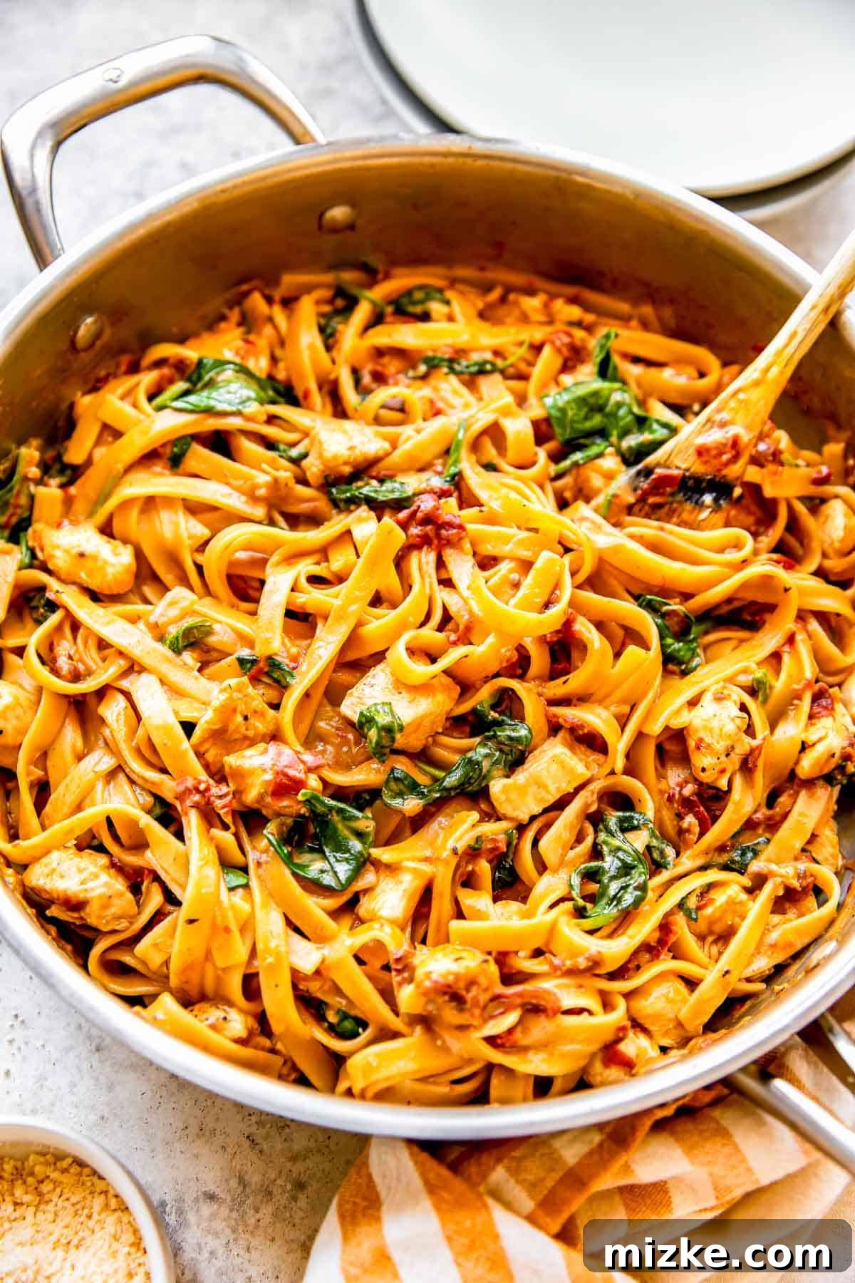 Sun-Kissed Skillet Chicken Pasta 12 The finished sun-dried tomato chicken pasta, artfully presented in a stainless steel skillet with a wooden spoon, resting beside a charming yellow striped linen towel