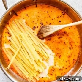 Sun-Kissed Skillet Chicken Pasta 19 Dry linguine pasta added to a stainless steel skillet with liquid and wooden spoon