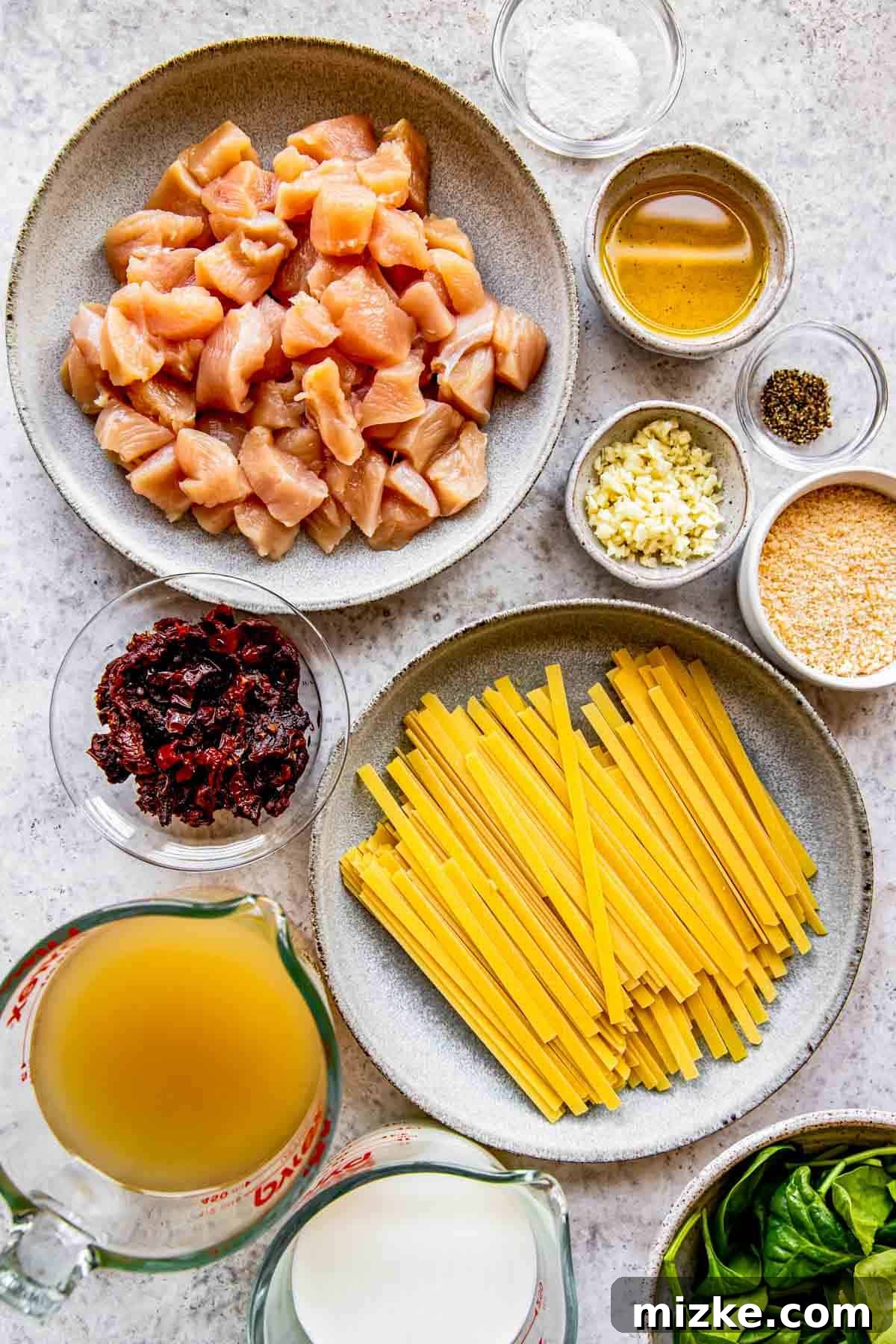 Sun-Kissed Skillet Chicken Pasta 3 A flat lay image displaying all the fresh ingredients for sun-dried tomato chicken pasta, including chicken breast, sun-dried tomatoes, garlic, spinach, milk, stock, and pasta