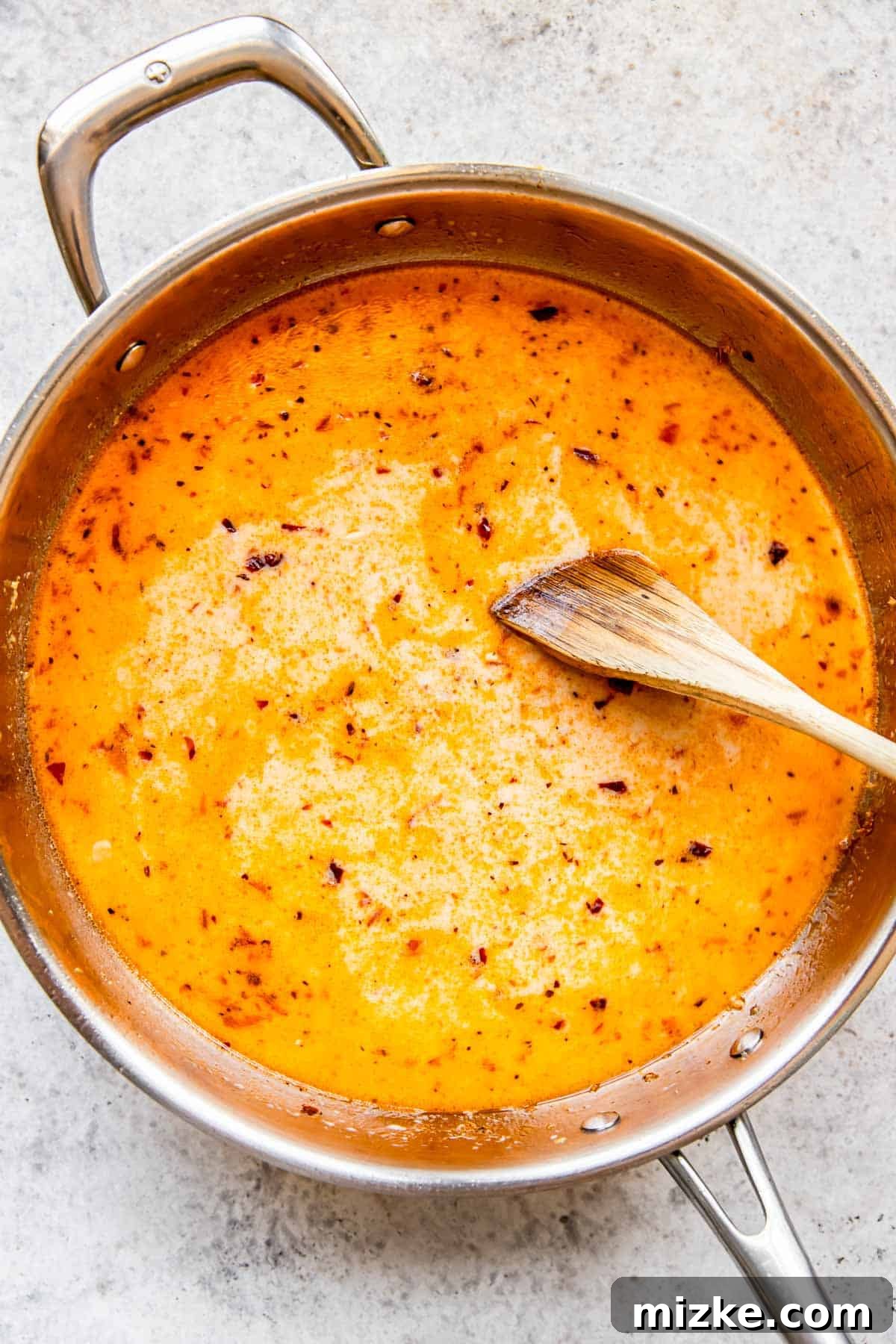 Sun-Kissed Skillet Chicken Pasta 8 Creamy liquid in a stainless steel pan being stirred with a wooden spoon, creating a smooth base for the pasta