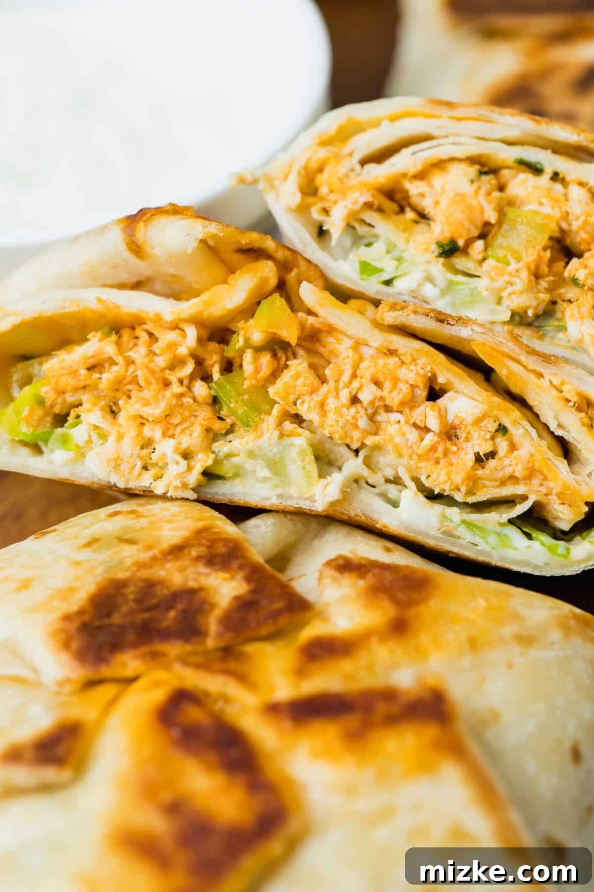 Two mini buffalo chicken crunchwraps on a cutting board, one cut in half to show the delicious filling of chicken, blue cheese, and lettuce.