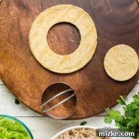 a 3” biscuit cutter cutting a circle in a corn tortilla on a wooden cutting board, preparing for frying