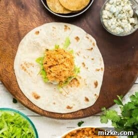 assembling the buffalo chicken crunchwrap on a large flour tortilla with dressing, lettuce, blue cheese, and chicken