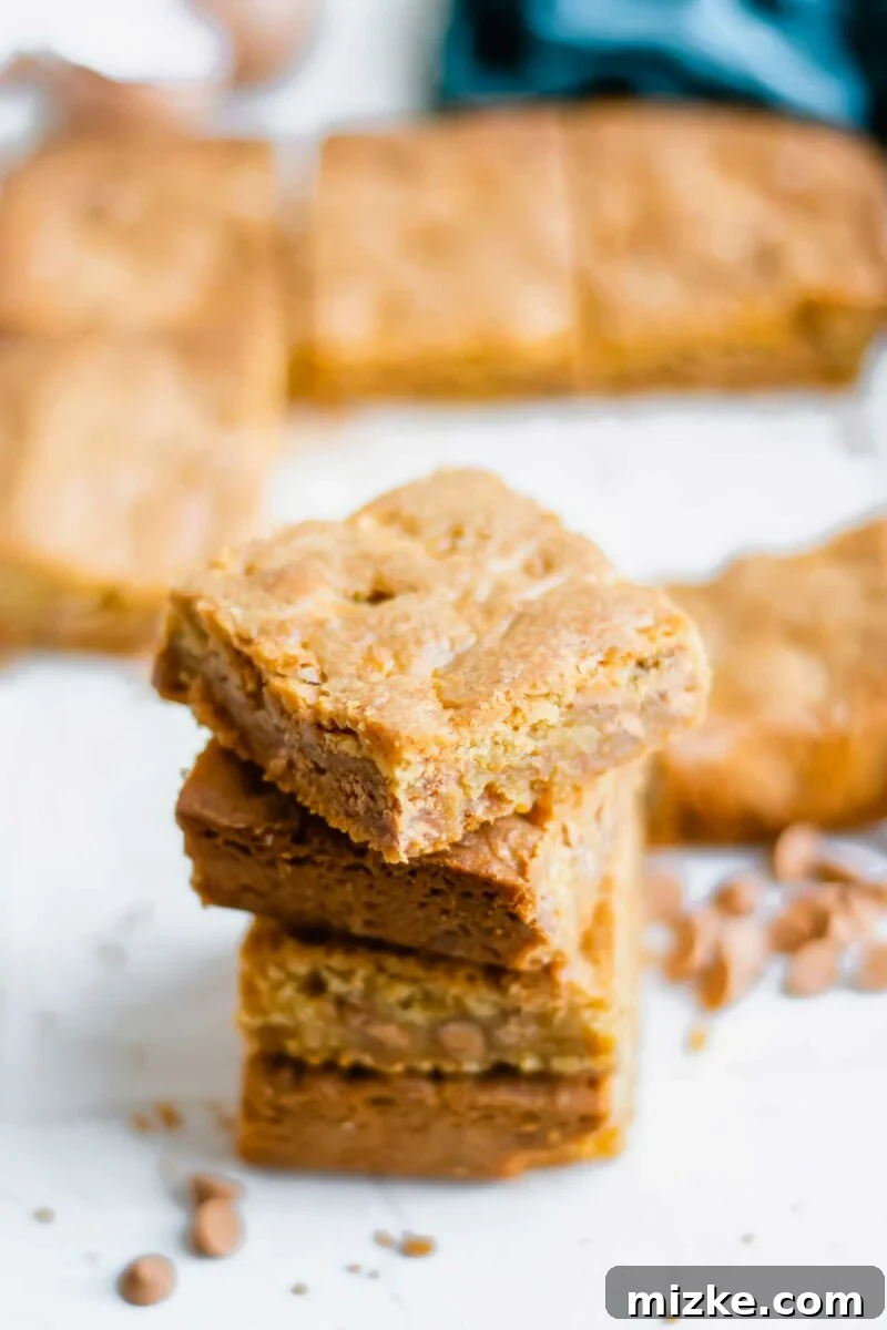 Golden Chewy Blondies 4 A beautifully stacked display of four butterscotch blondies, with a scattering of butterscotch chips around them, highlighting their appealing texture.