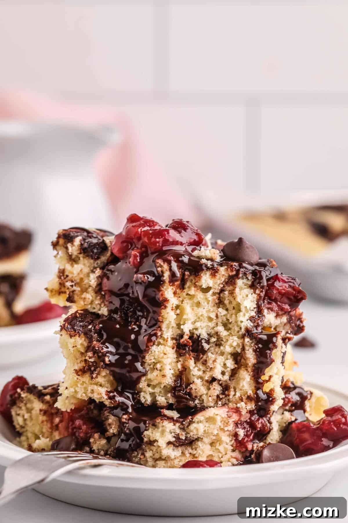 Chocolate Cherry Pancake Bake 2 Stacked squares of chocolate cherry sheet pan pancakes in a bowl, drizzled with chocolate sauce and garnished with tart cherries