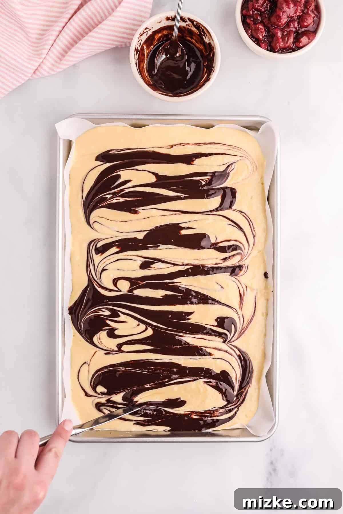 Chocolate Cherry Pancake Bake 6 Chocolate sauce being swirled artistically into the pancake batter on a sheet pan using a butter knife
