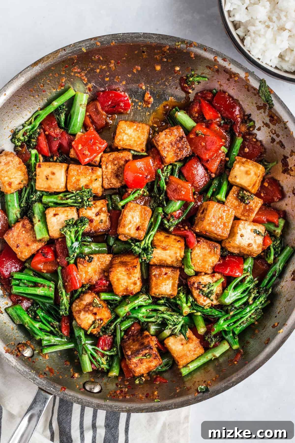 Crispy Tofu Stir-Fry 11 The vibrant spicy chili tofu stir fry, glistening with its rich lava sauce, is actively being cooked and tossed in a large skillet, ready to be served.
