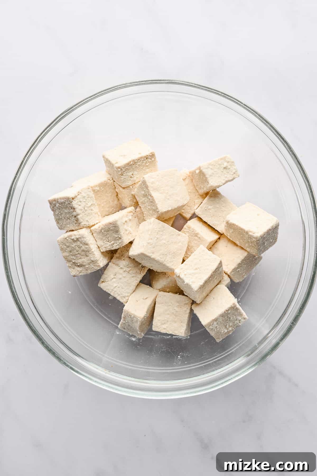 Crispy Tofu Stir-Fry 7 Perfectly cubed tofu pieces are evenly coated with a delicate layer of cornstarch, ready to be cooked for maximum crispiness, in a clear glass bowl.