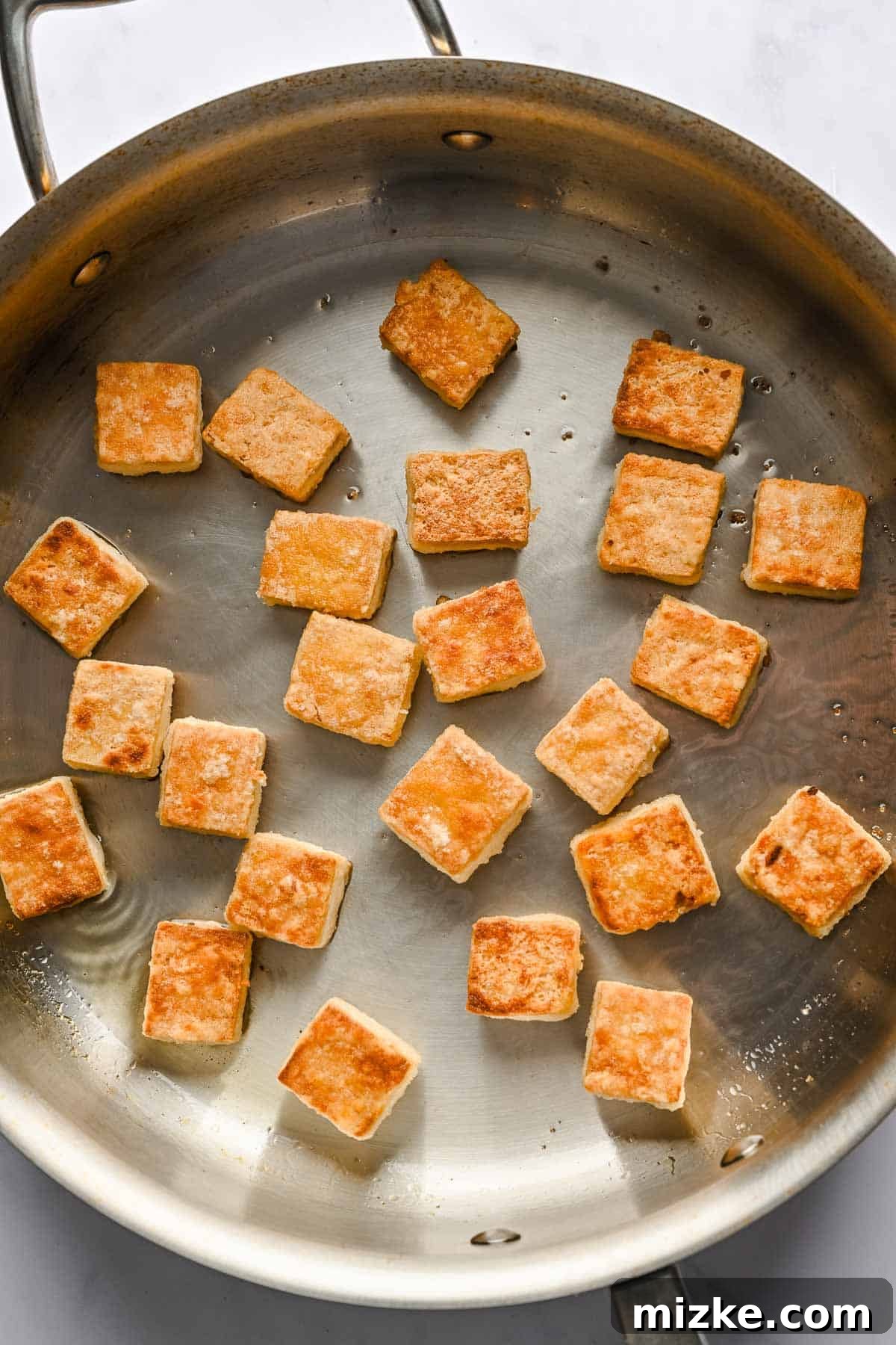 Crispy Tofu Stir-Fry 8 Golden-brown, crispy tofu cubes sizzle enticingly in a metal skillet, having achieved a perfect crust through careful cooking.