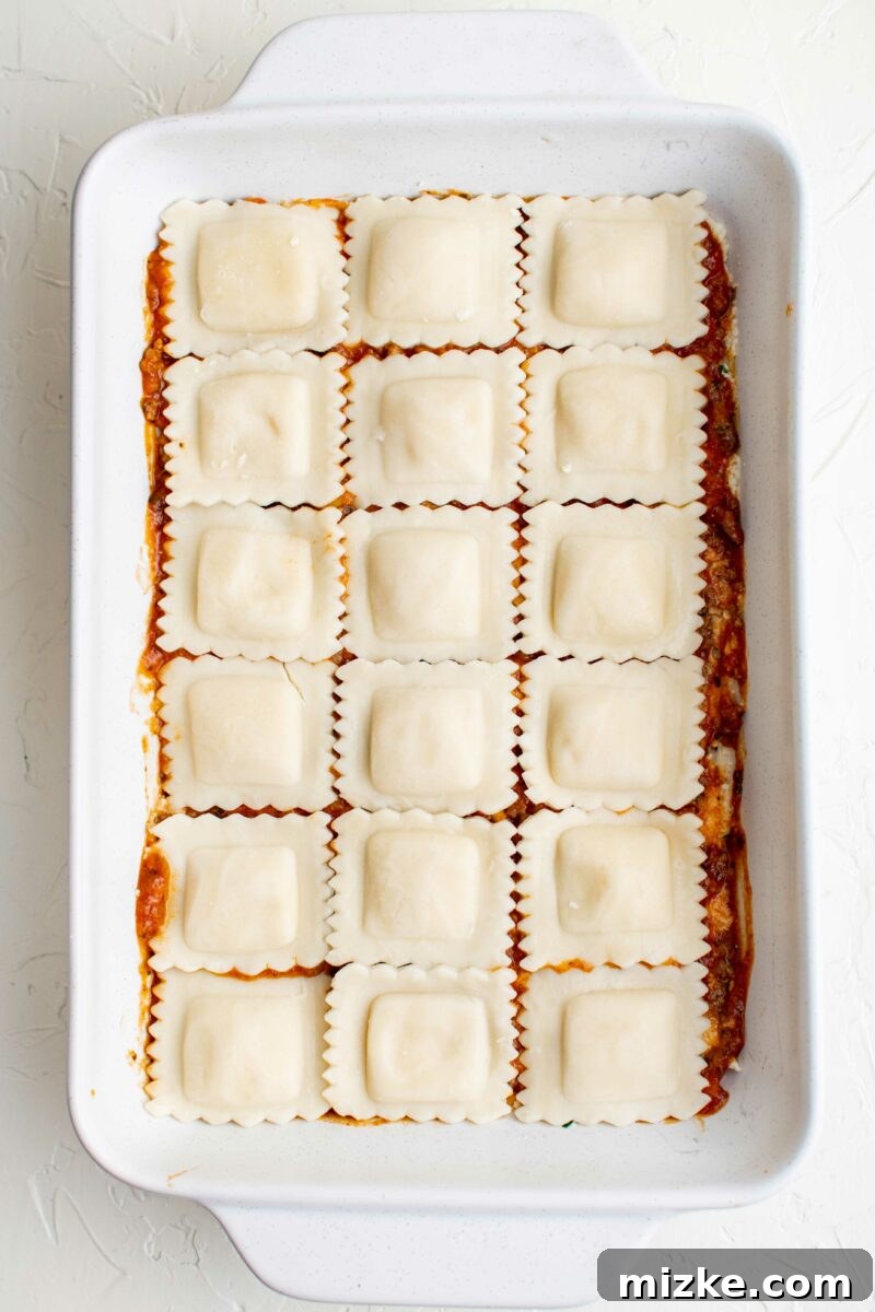 Ravioli Lasagna Bake 7 A layer of cooked ravioli is perfectly placed on top of red sauce in a baking dish, ready for more layers.