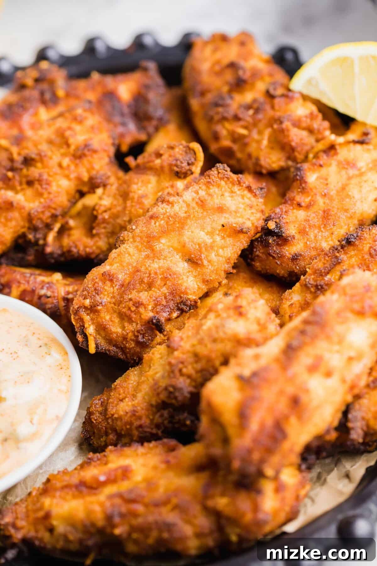 Crispy Air Fryer Fish Sticks 8 A lemon wedge is placed at the edge of a serving platter filled with fish sticks.