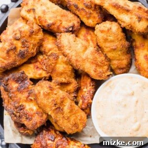 A number of crispy fish sticks are on a large serving platter with a small bowl of creamy cajun dipping sauce.