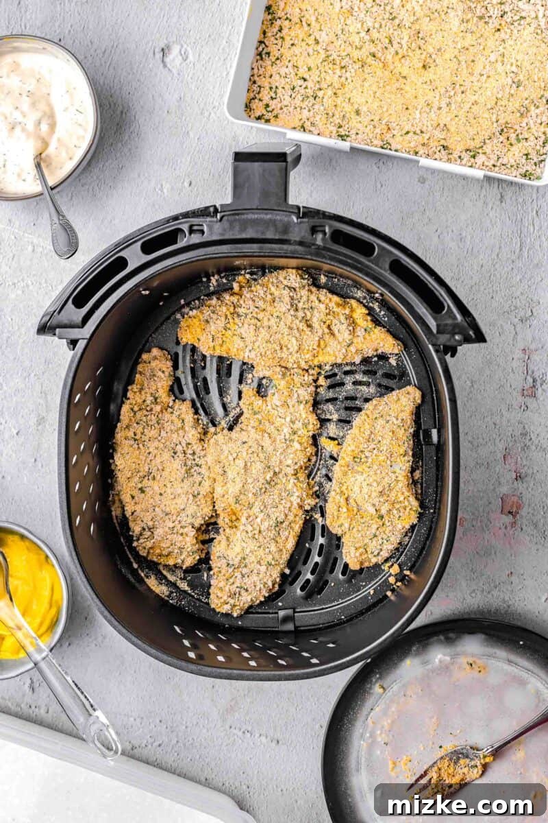 Crispy Golden Air Fryer Catfish 6 Four pieces of breaded catfish fillets neatly arranged in an air fryer basket, ready for cooking.