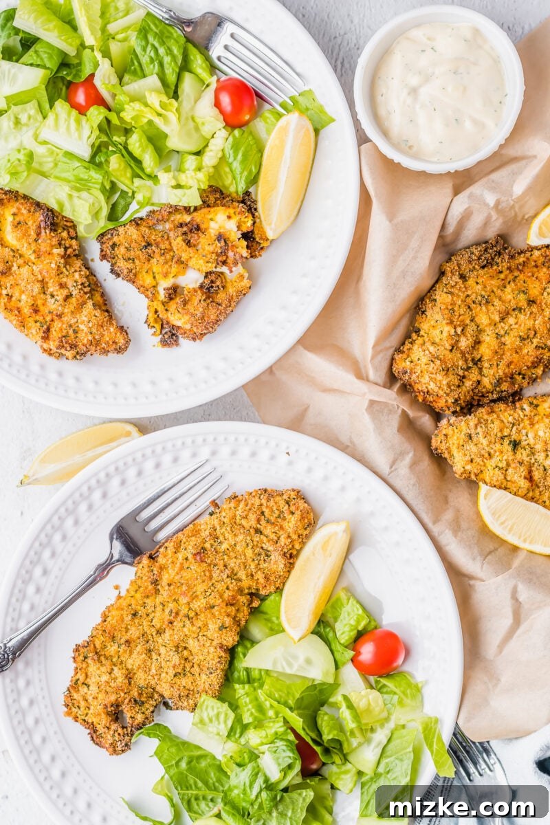 Crispy Golden Air Fryer Catfish 10 Two white plates featuring servings of crispy air fryer catfish, fresh lemon wedges, and a side salad.