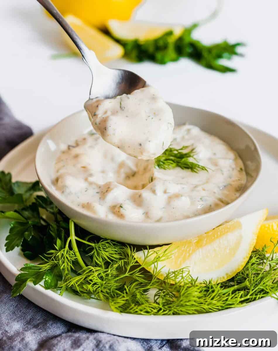Fresh and Zesty Tartar From Scratch 3 A metal spoon gracefully lifts a generous portion of creamy homemade tartar sauce from a full bowl, highlighting its perfect texture.