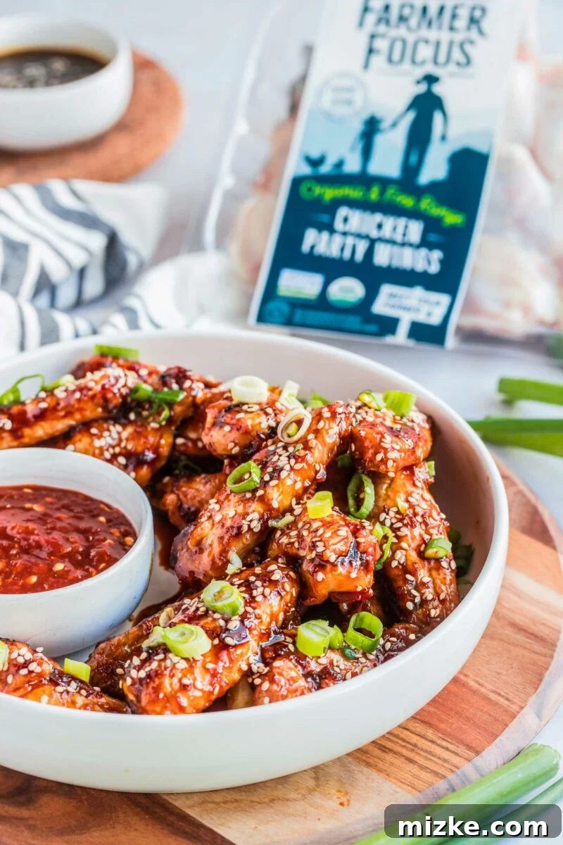 Gochujang Glazed Wings 4 A medium-sized white serving bowl holds a generous portion of chicken wings, beautifully garnished with toasted sesame seeds and freshly chopped green onions, ready to be served.