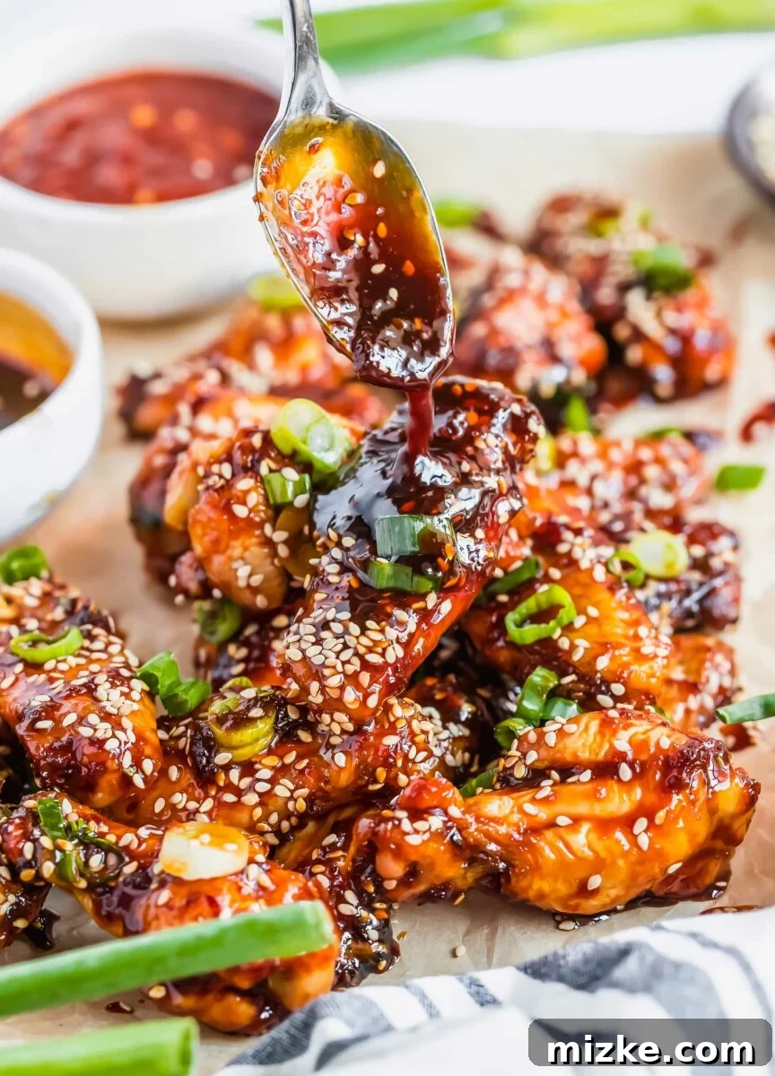 Gochujang Glazed Wings 5 A stream of homemade sticky sauce is being generously drizzled over a perfectly cooked chicken wing, highlighting its glossy texture.