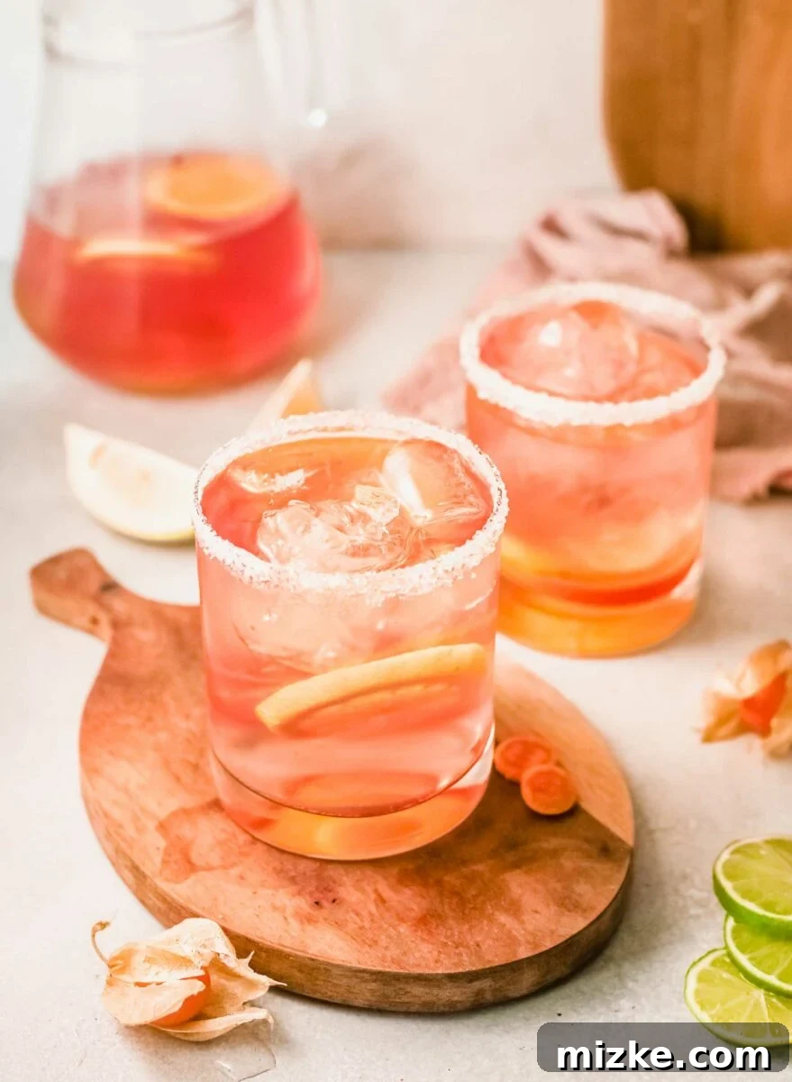 Sun-Kissed Rosé Sangria 2 Two glasses of pink sangria are placed next to a full pitcher filled with citrus slices.