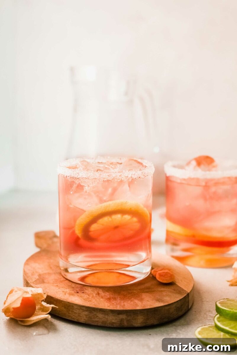 Sun-Kissed Rosé Sangria 3 A hand reaches for a glass of pink sangria next to a pitcher filled with citrus slices.