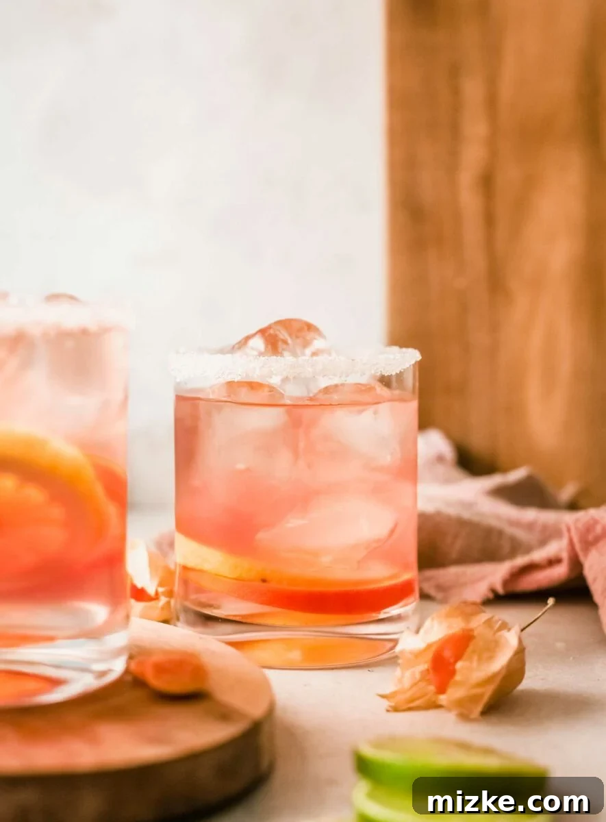 Sun-Kissed Rosé Sangria 4 A glass of citrus rosé sangria, sugar-rimmed and filled with ice cubes and fruit slices, sits on a surface.