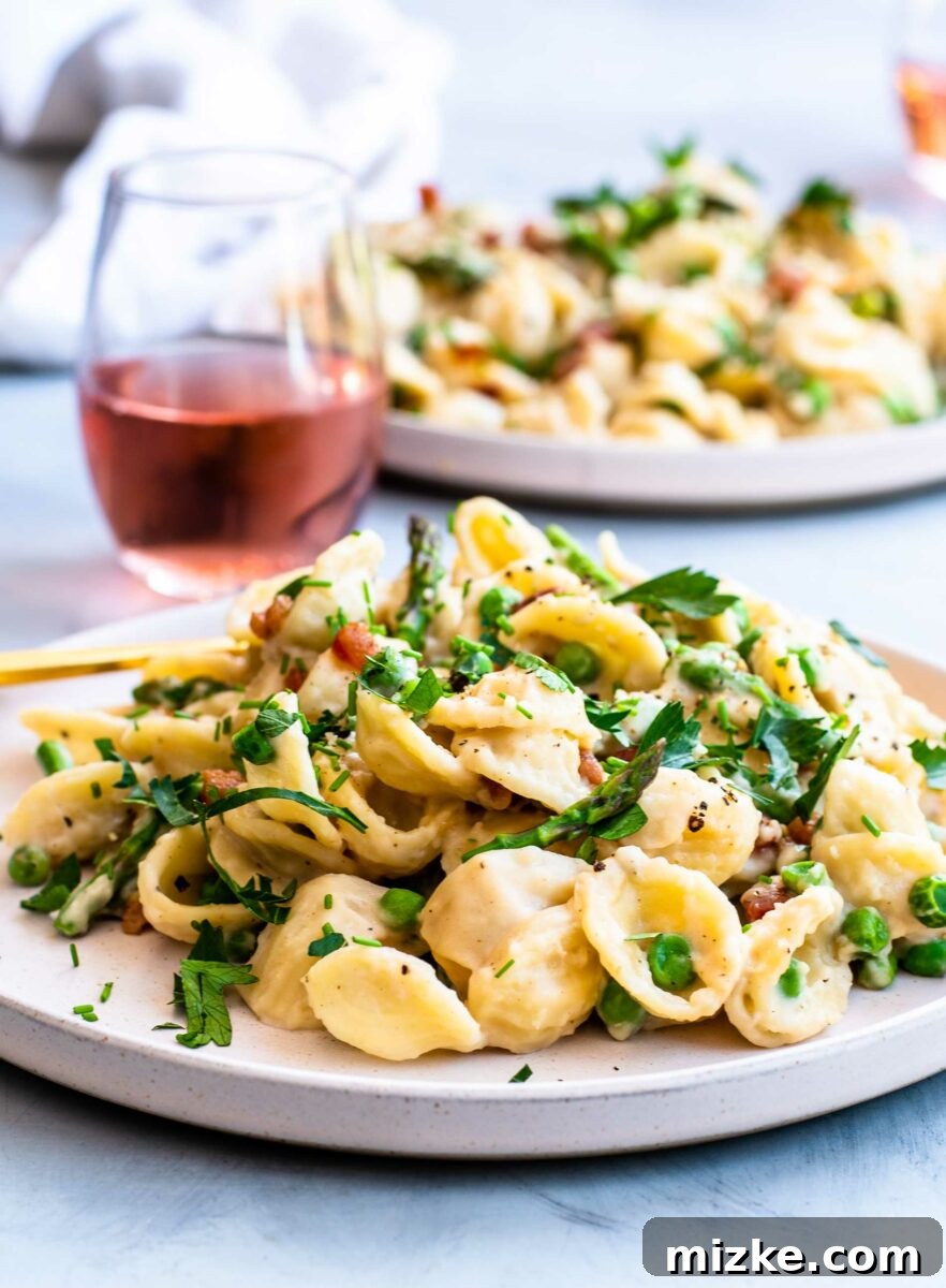 A glass of rosé is pictured in the background of a full plate of pasta with asparagus, peas, and pancetta.