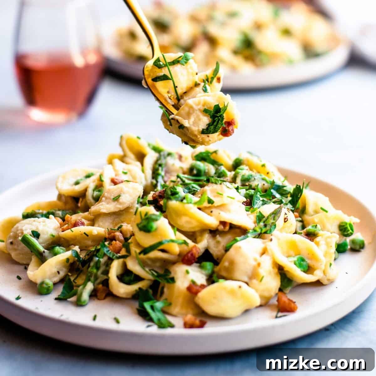 A fork is lifting a bite sized portion of noodles and veggies from the plate of creamy pasta.