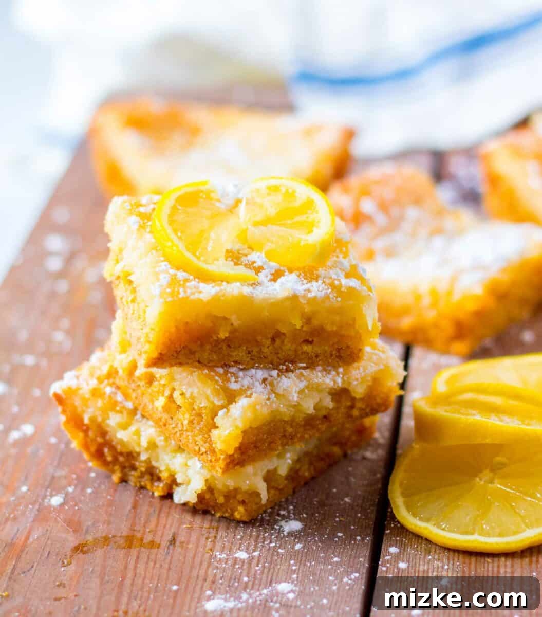 Luscious Lemon Gooey Butter Cake 2 A few pieces of lemon cake are stacked on top of one another on a wooden surface.