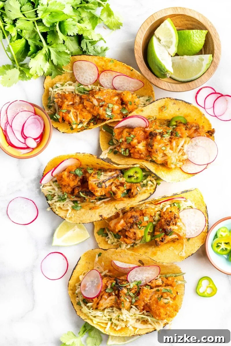 Five vibrant cauliflower tinga tacos, beautifully arranged and garnished, are presented on a clean white surface, showcasing their delicious fillings and inviting appearance.