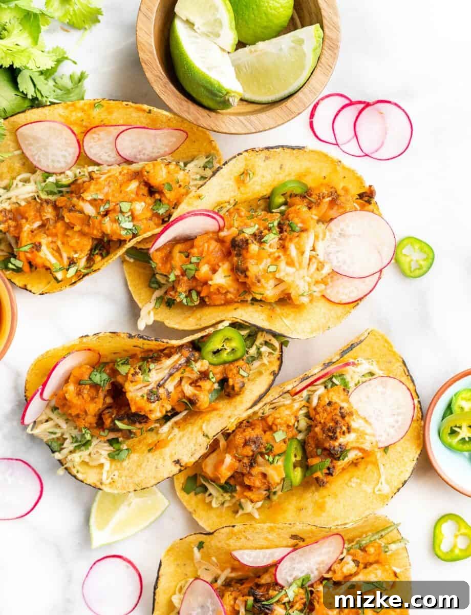 A beautifully arranged serving of ready-to-eat cauliflower tinga tacos, complete with fresh garnishes, rests on a white surface, inviting one to indulge.