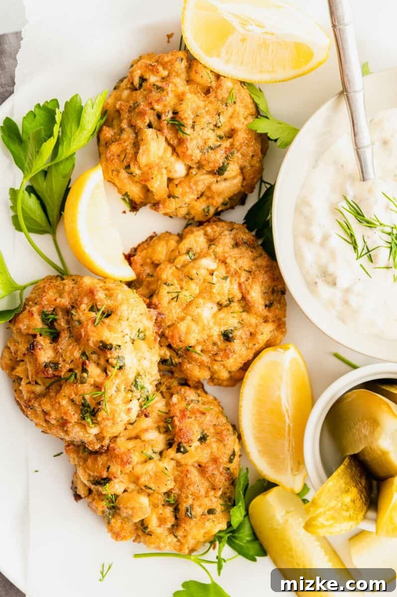 Ultimate Crab Cake Sandwiches 2 Four golden-brown crab cakes, perfectly seared, are elegantly arranged on a crisp white plate, garnished with vibrant fresh herbs, promising a gourmet experience.